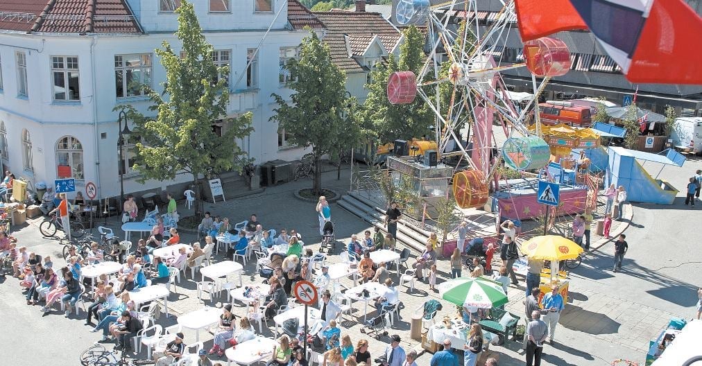 Aerial view of a busy outdoor street fair with white vendor tents, crowds of visitors, surrounding buildings, and red signage